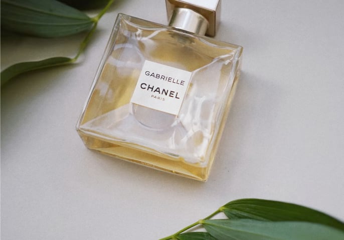 Gabrielle Essence Parfum bottle laying down with leaves surrounding